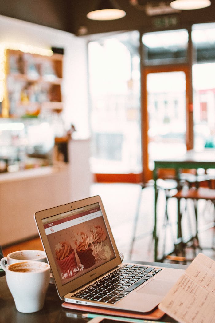 A cozy café setting with a laptop, coffee, and notebook, perfect for working or blogging.