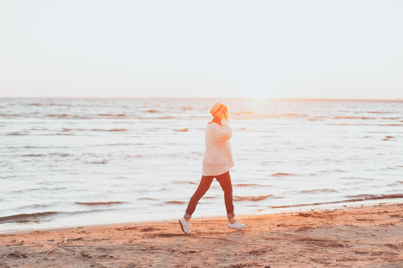 A woman enjoys a peaceful walk along the beach during sunset, capturing a serene summer moment.