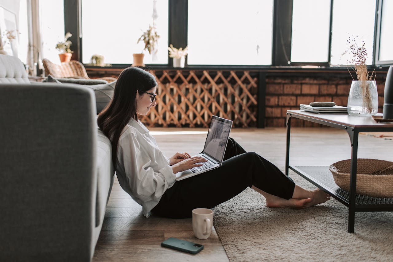 A young woman working from home using a laptop in a relaxed living room setting.